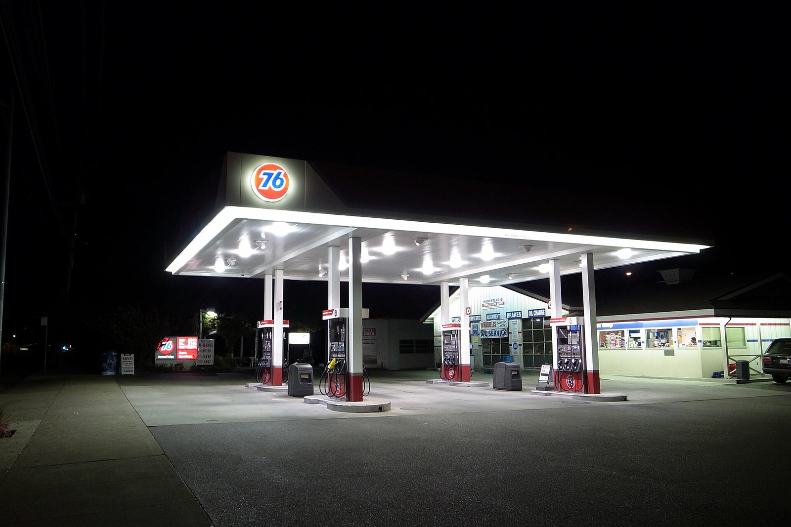 A 76 petrol station forecourt at night, its canopy lit against a dark sky, pumps standing empty