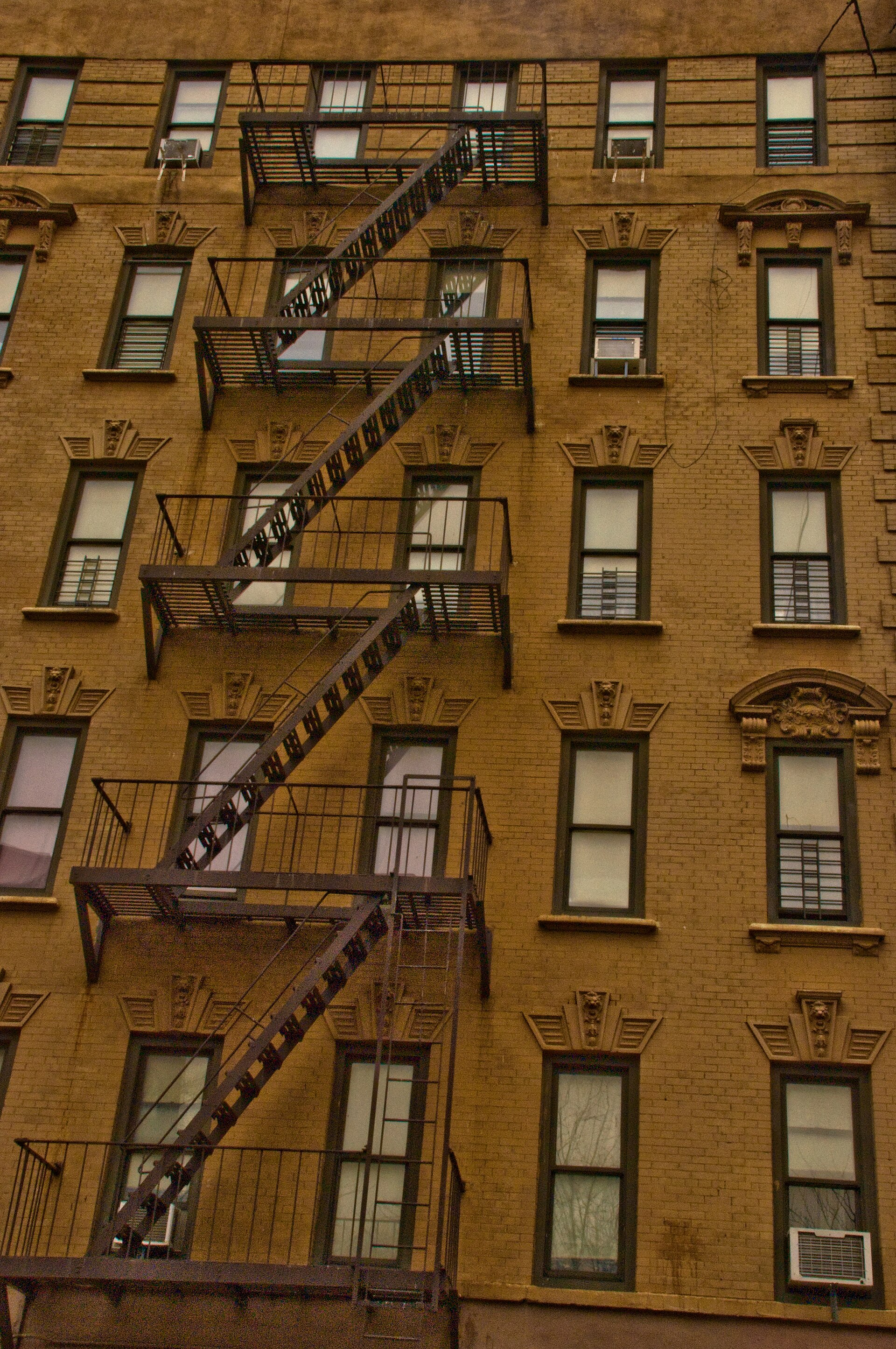 A block of brick apartment buildings on 143rd Street in the Bronx, windows in rows, cars parked below
